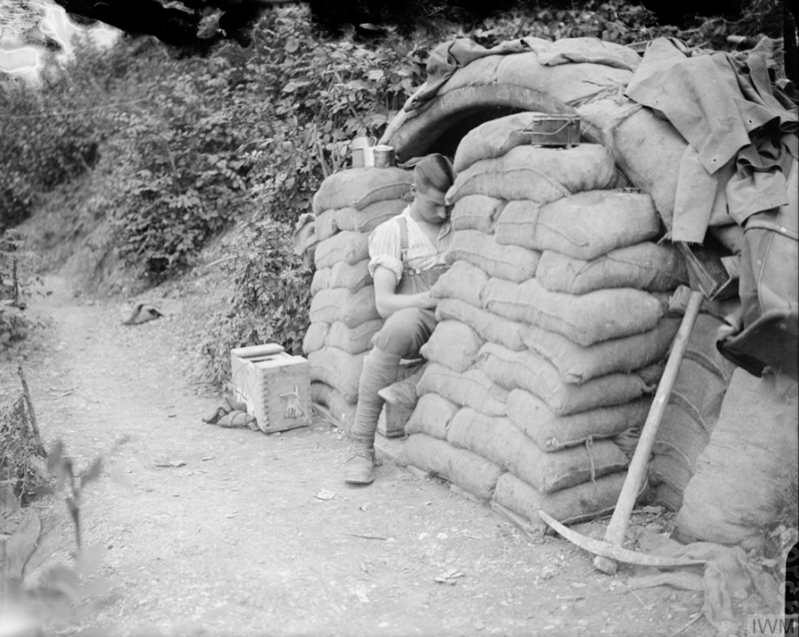 A soldier reading at the entrance to his dug-out, reinforced with sandbags. Fampoux, 21 July 1917. © IWM Q 5702
