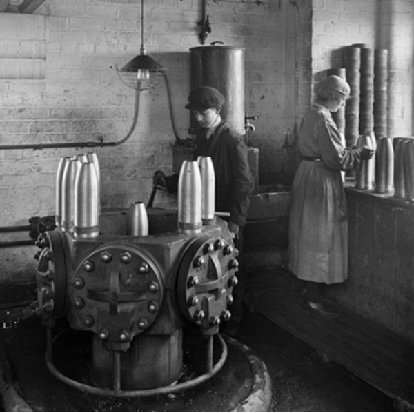 Cunard Shell Works, Rimrose Road, Bootle, Sefton, 1917 Historic England Archive BL24001/099 Reproduced by permission of Historic England A boy worker operates a hydraulic press to fix copper driving bands onto the shells. Behind him, a female worker fits a band to a shell before it is goes into the press© The Historic England Archive, Historic England (2022)