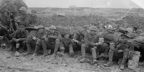 Canadian troops eating rations whilst seated on muddy ground outside a shelter near Pozieres during the final stages of the Battle of the Somme, October 1916