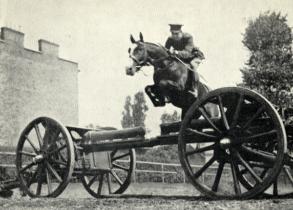 St. John's Wood Barracks. 1917 Lt & Riding Master J.E.Hance of the RHA training brigade demonstrating jumping tchniques over the guns and a wire fence in the manege at St John's Wood Barracks