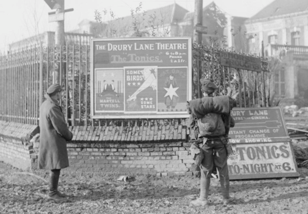 British soldiers looking at theatre posters in Bapaume advertising 'The Tonics' concert party, 30 January 1918 (c) IWM Q 10644