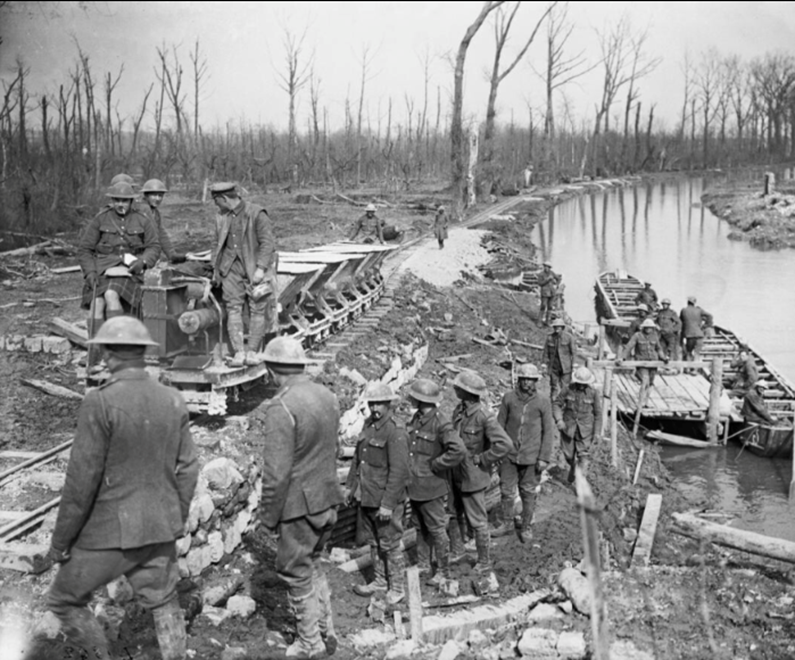Gunners of the Royal Artillery loading pontoons on the River Scarpe with shells whilst a light railway engine passes along the line near Saint-Laurent-Blangy, 22 April 1917. (c) IWM Q5828